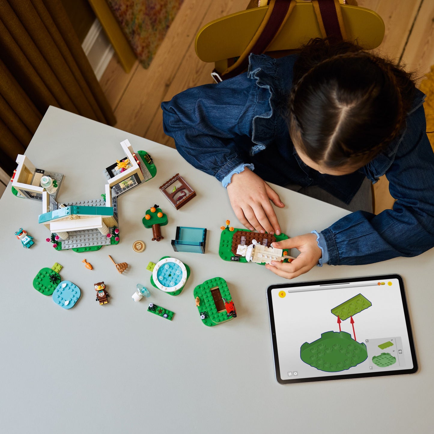Child building a LEGO set on a table with various colorful pieces and a tablet nearby