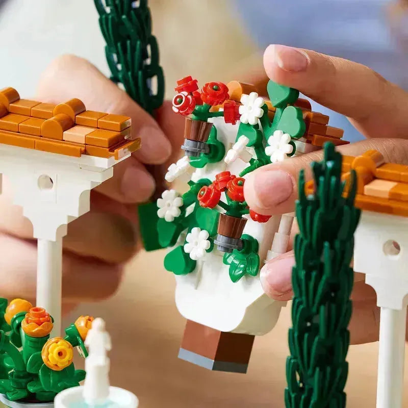 Close-up of hands building a colorful Lego botanical garden with flowers and accessories